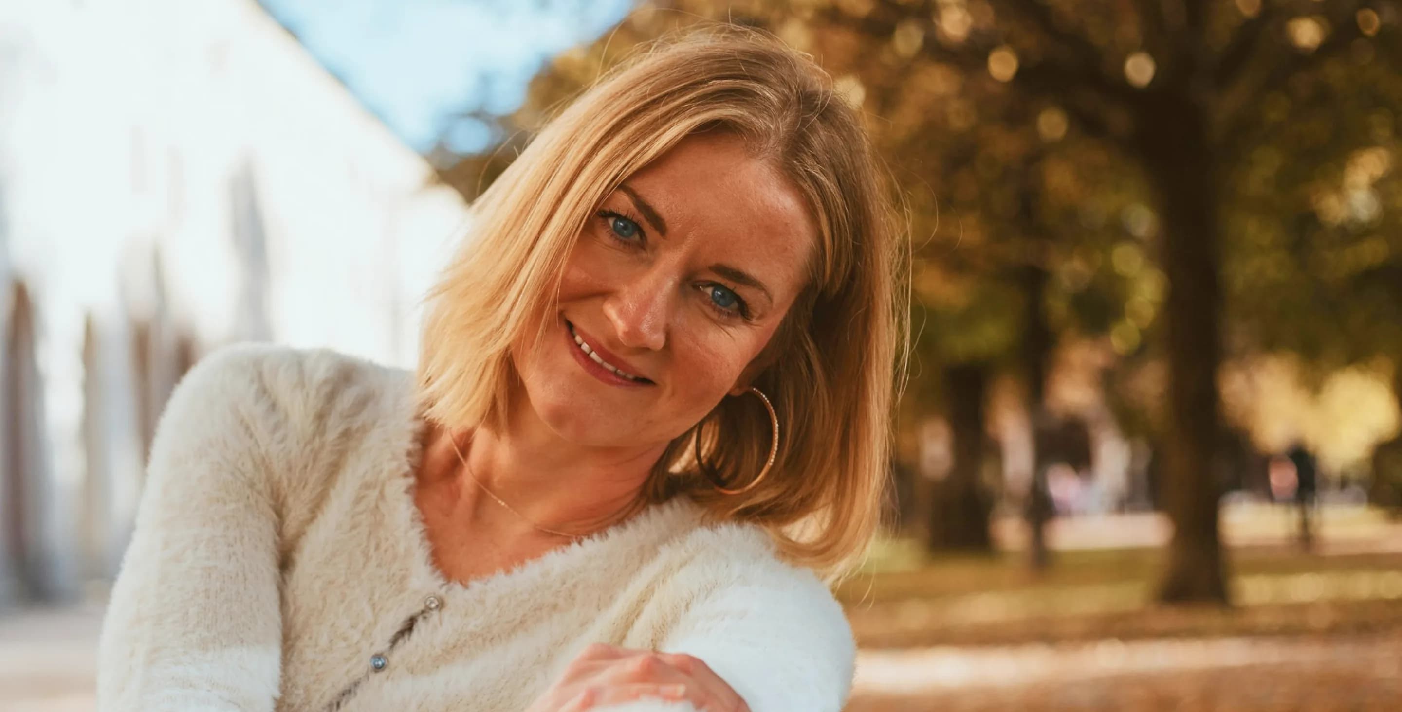 Smiling woman with shoulder-length blonde hair in an autumn park