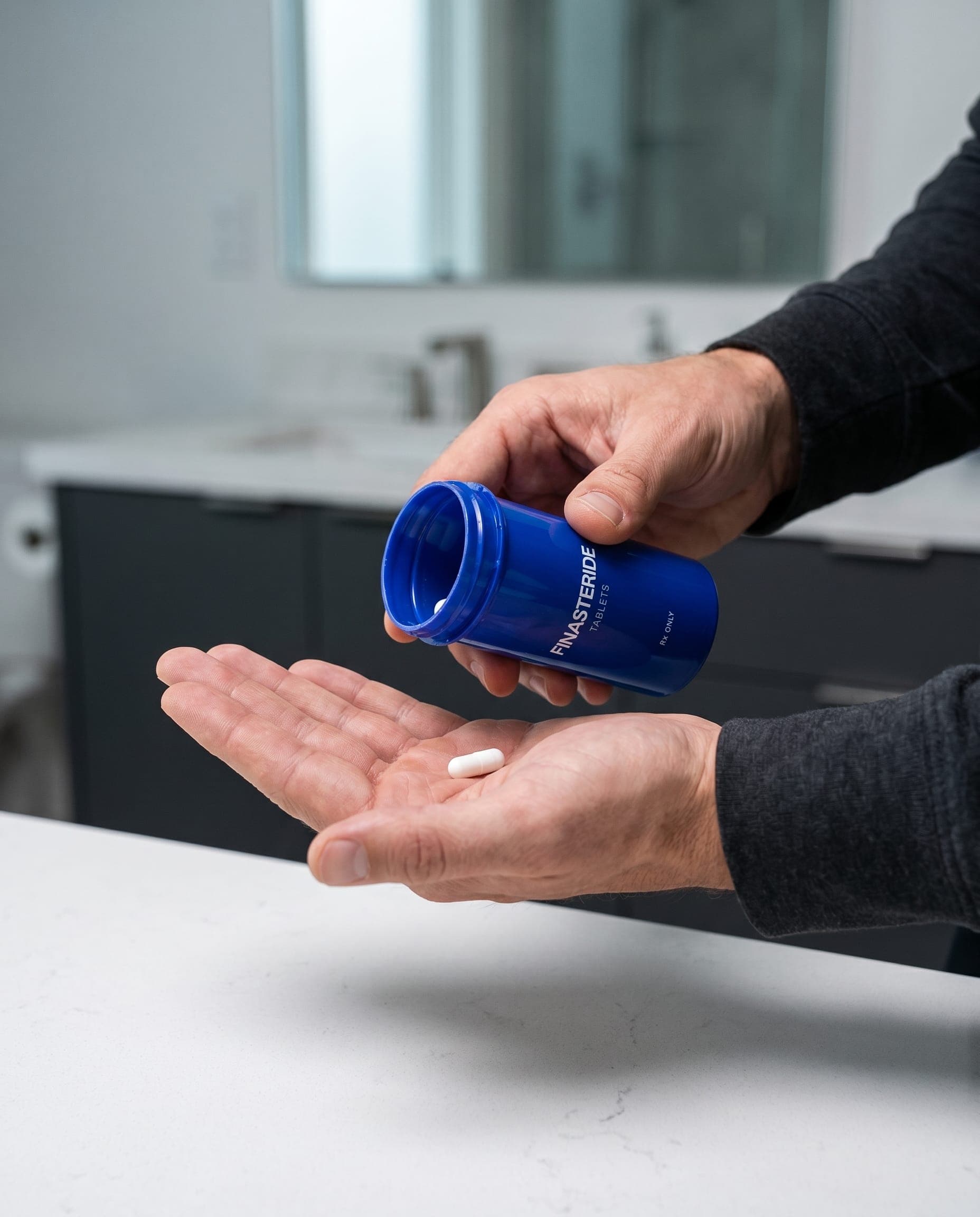 Hand pouring a Finasteride tablet onto a palm, bathroom counter