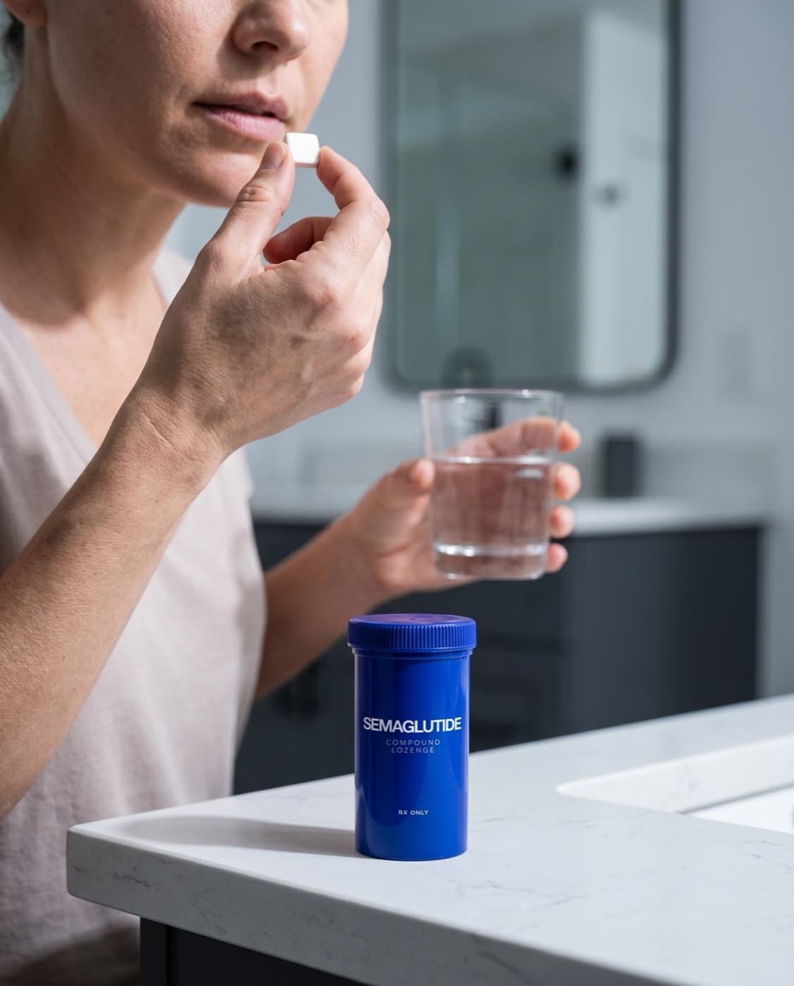 Person taking a compounded Semaglutide lozenge with a glass of water