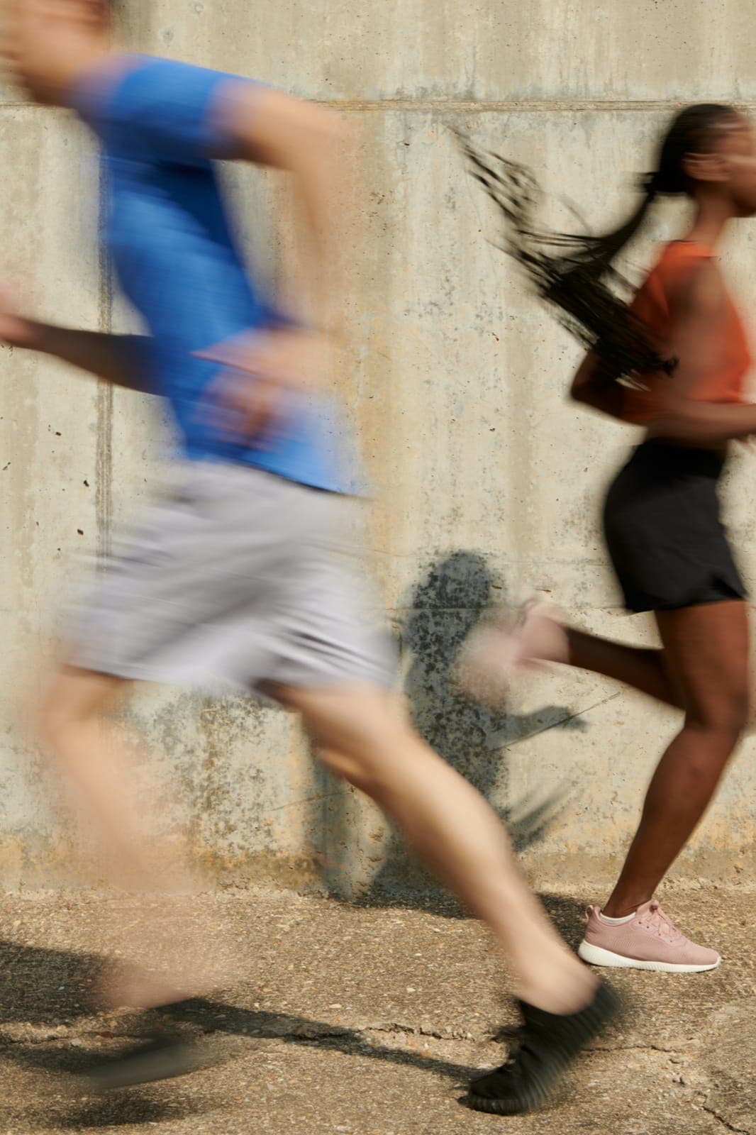 Two people running past a concrete wall