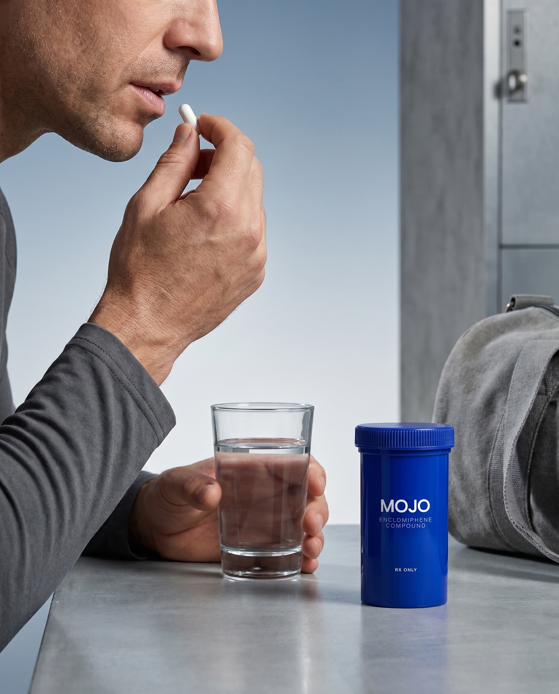 Man taking an Enclomiphene capsule with a glass of water next to a Mojo bottle
