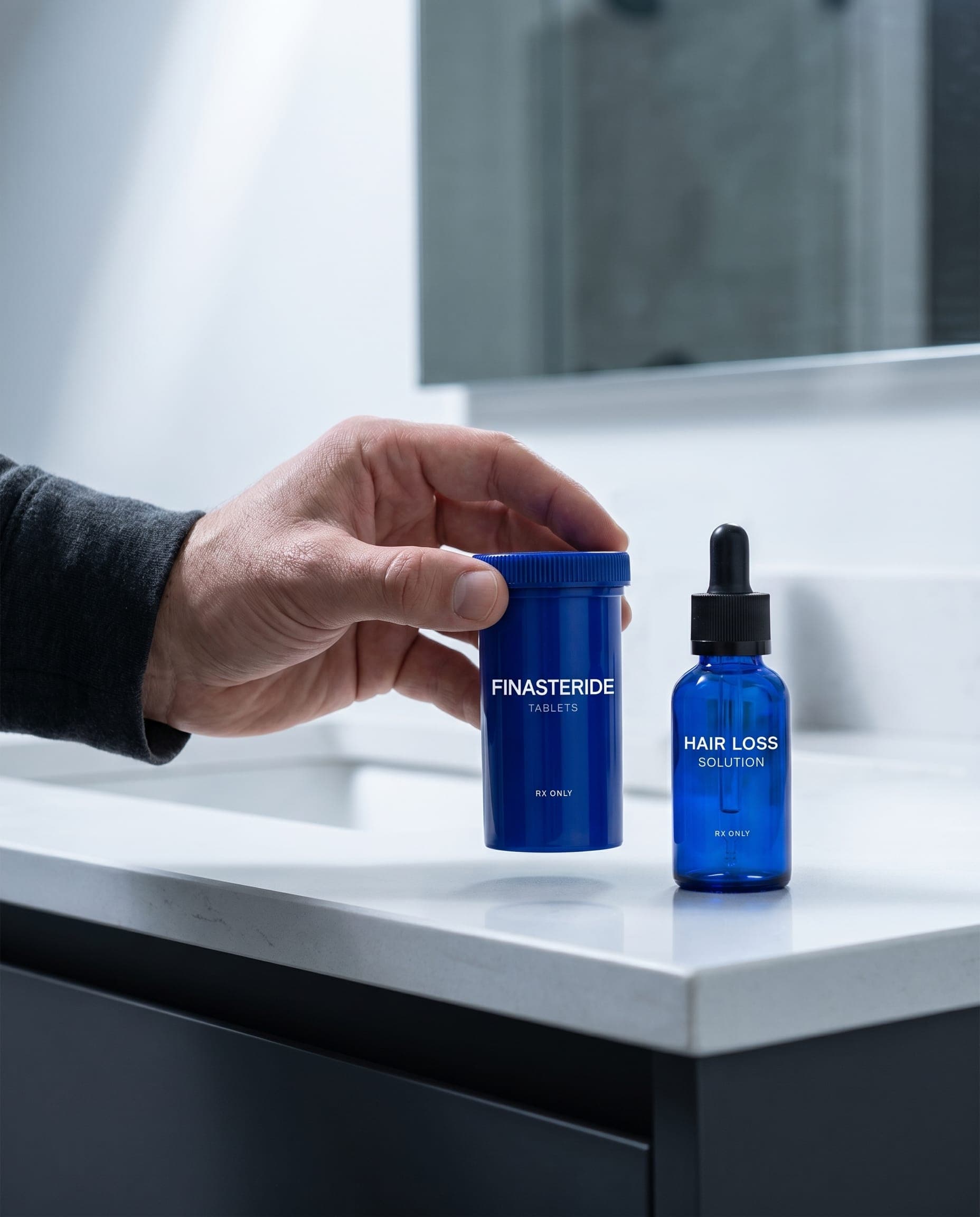 Hand picking up a Finasteride Tablets bottle next to a Hair Loss Solution dropper bottle