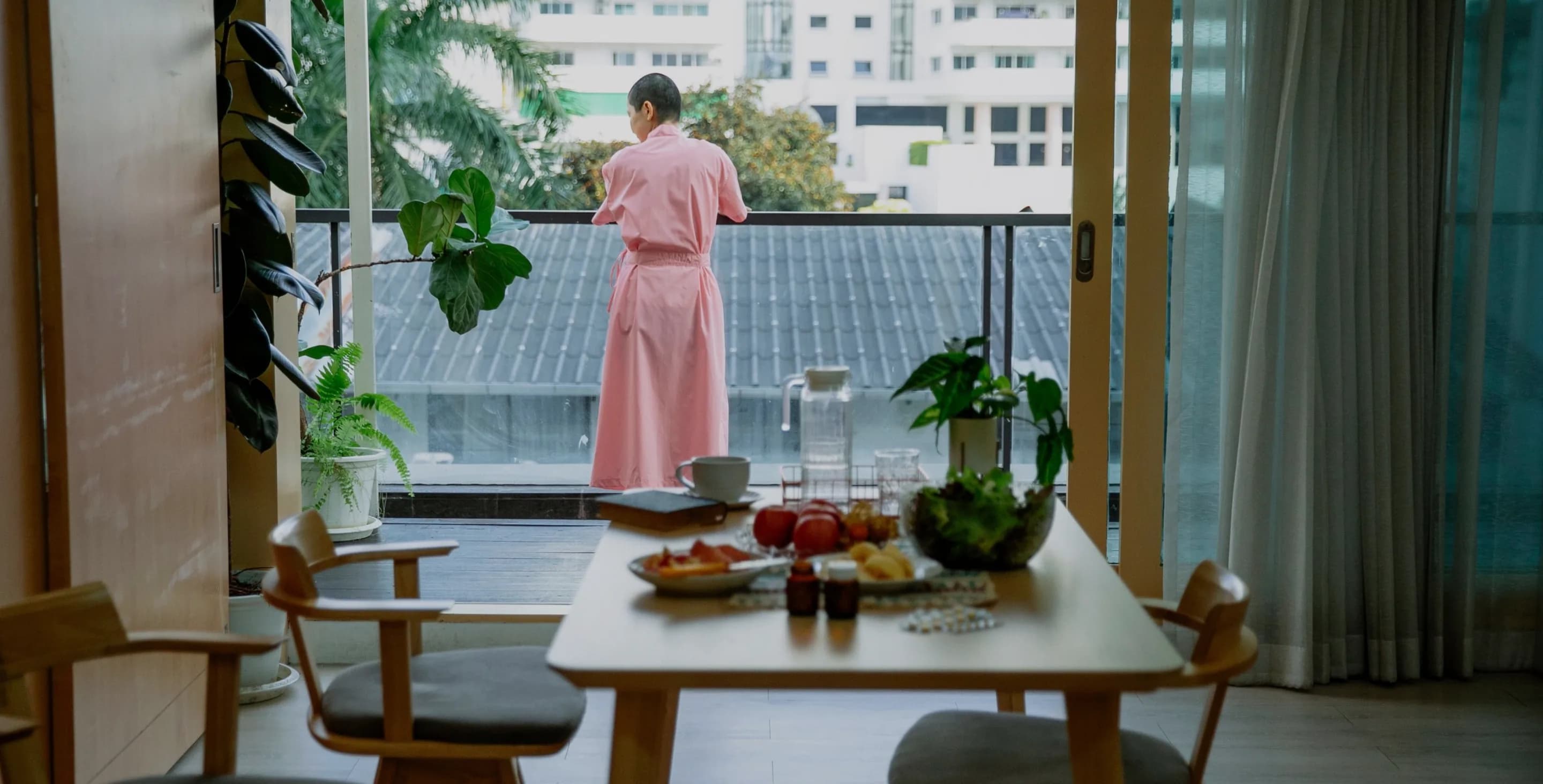 Person in a pink robe on a sunny balcony, breakfast table in the foreground