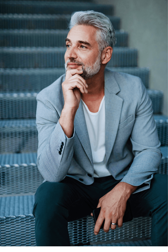 Man in a grey blazer sitting on stairs, hand on chin