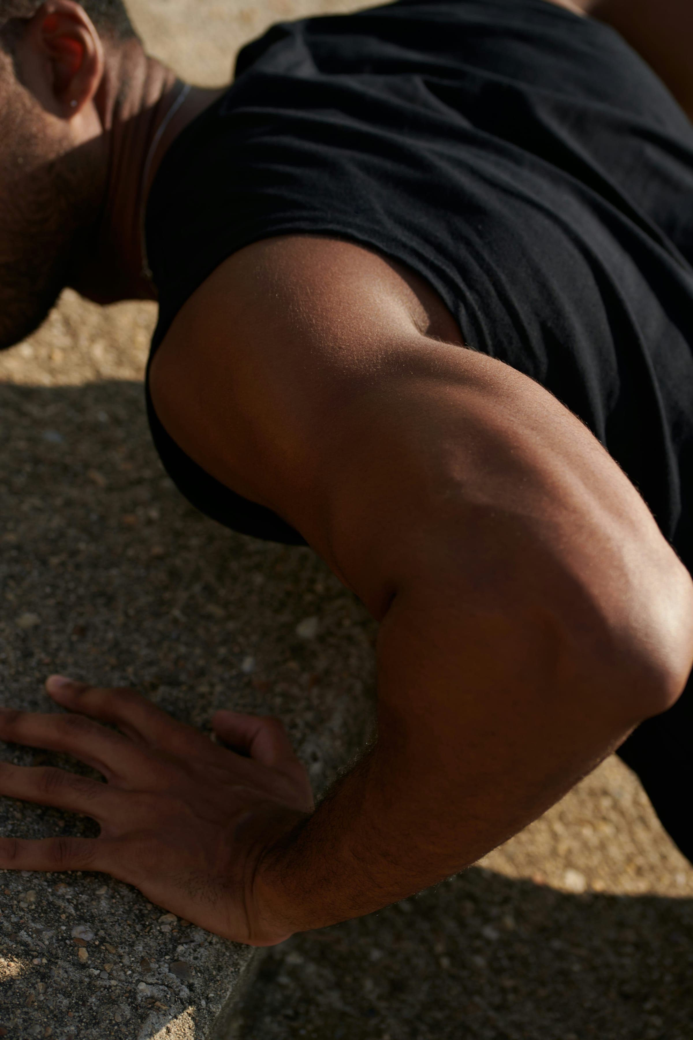 Man's shoulder and arm in dark clothing on rocky outdoor ground