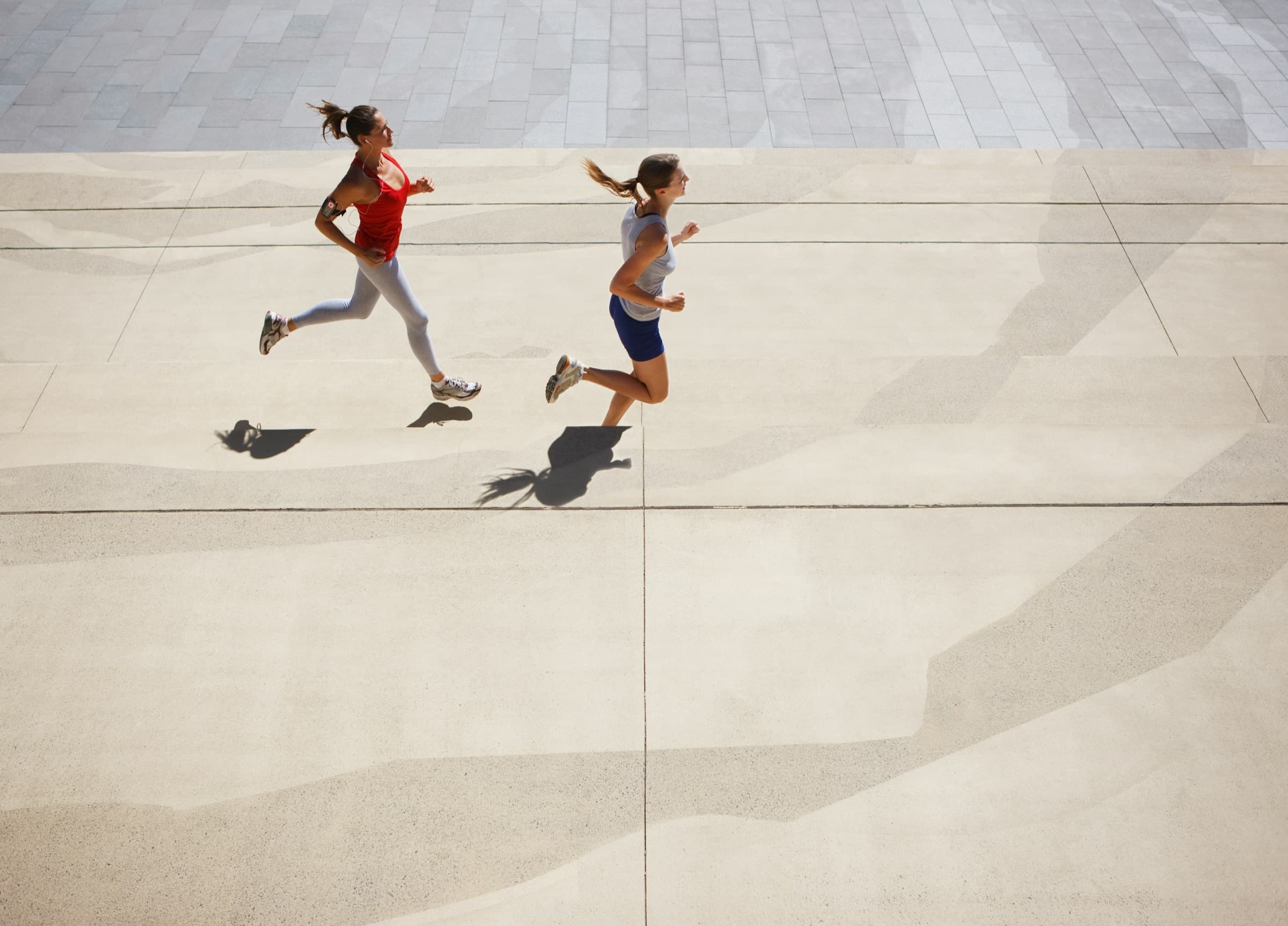 Two women jogging together on a stone plaza
