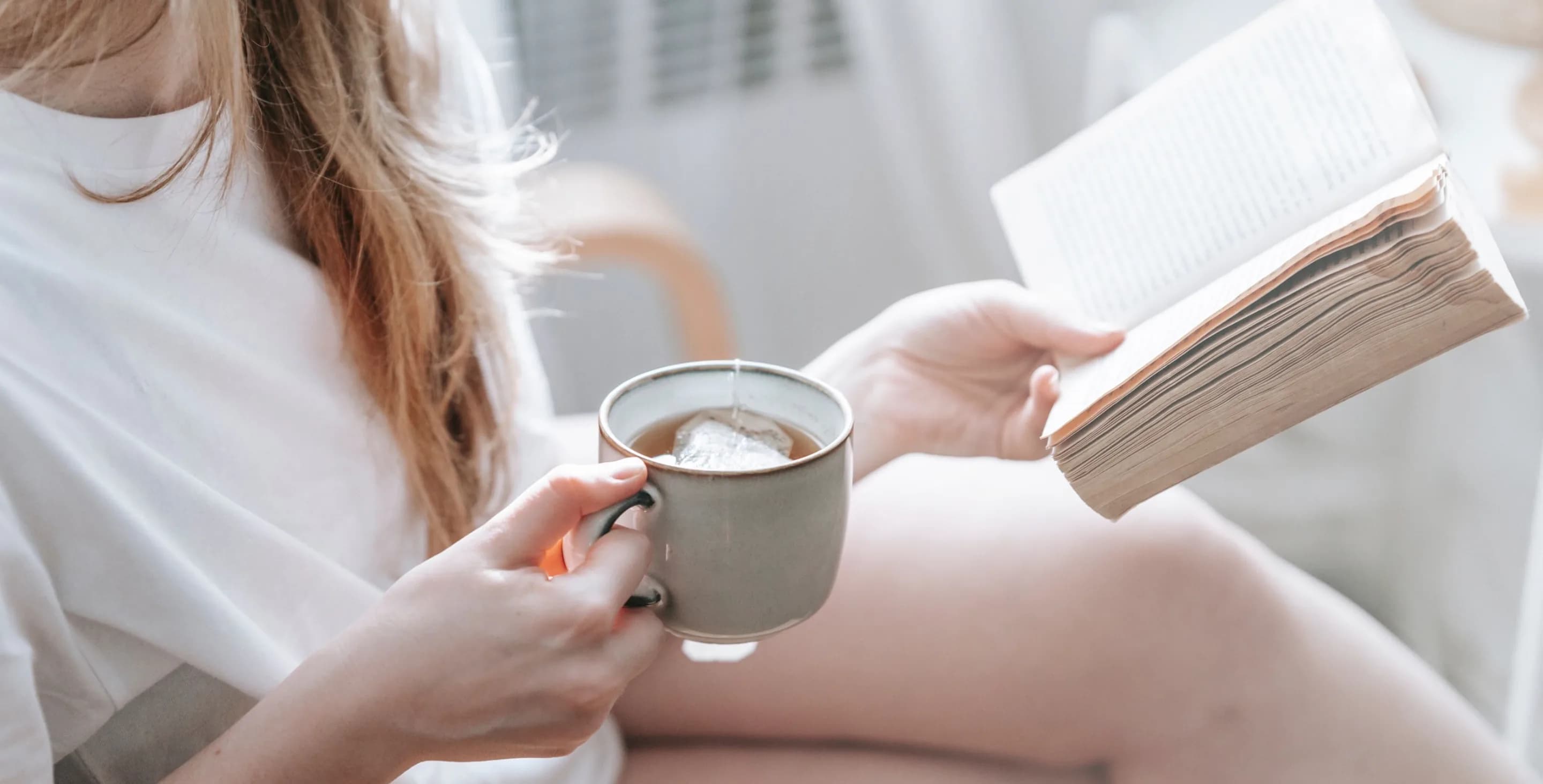 Person reading a book with a cup of tea