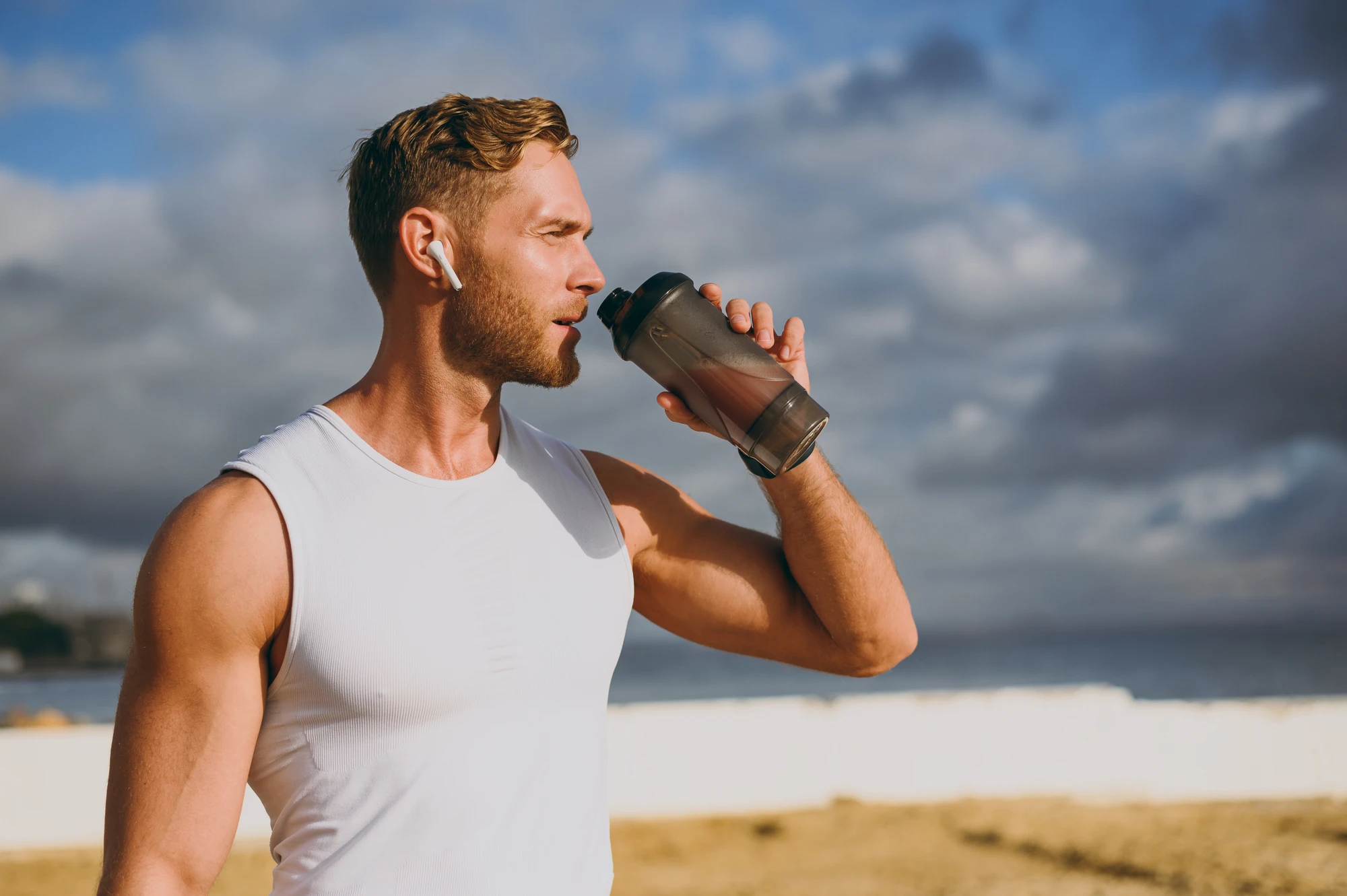 Man drinking from a shaker bottle outdoors